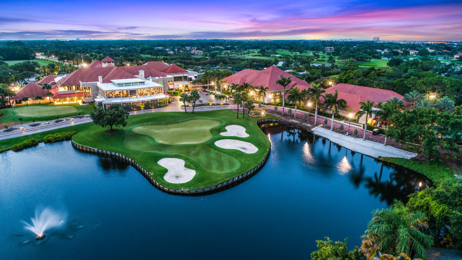 Aerial view of a South Florida golf club community at dusk, with clubhouse, green and lake