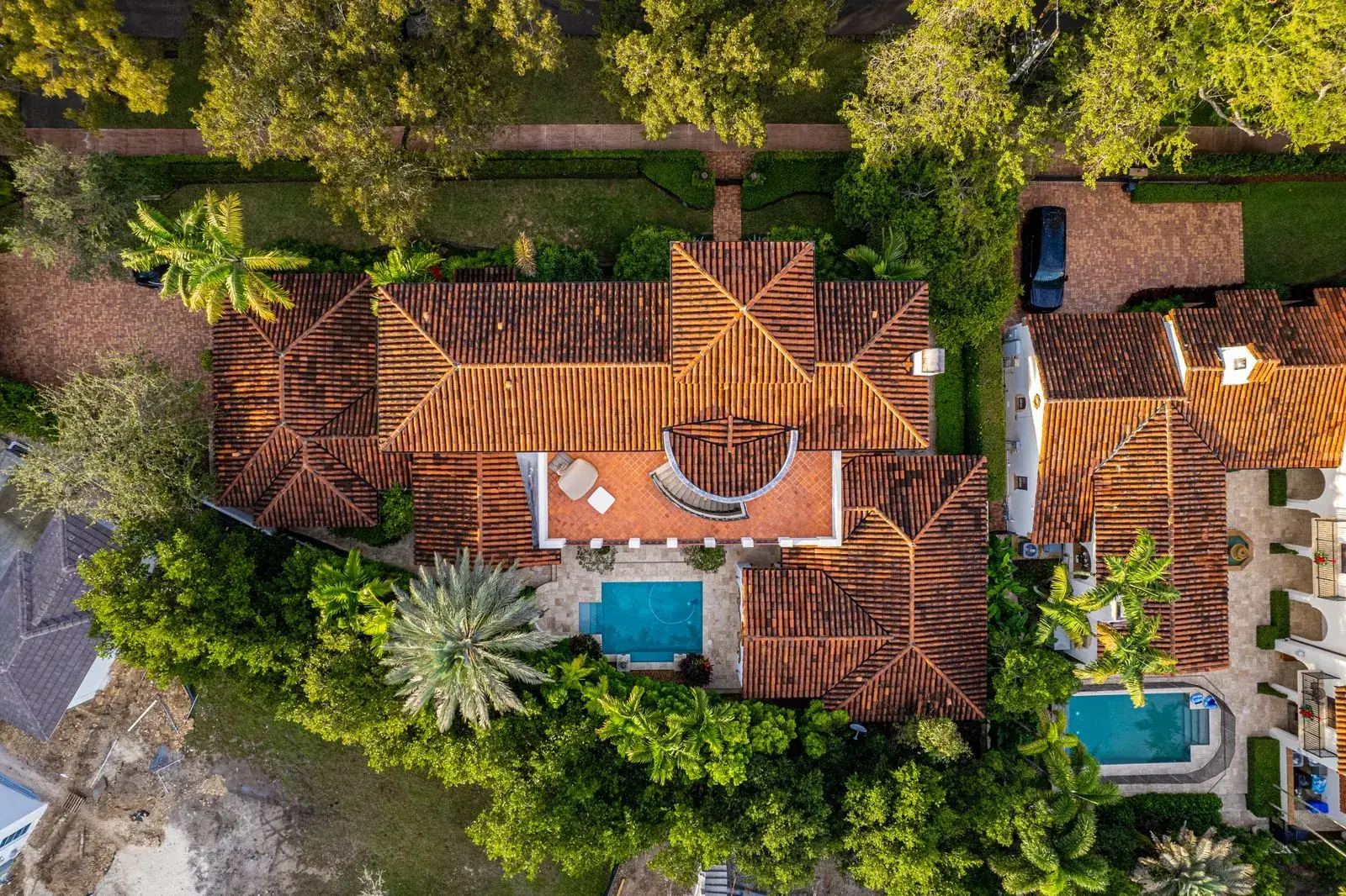 Aerial view of tile-roof homes with pools in a leafy neighborhood